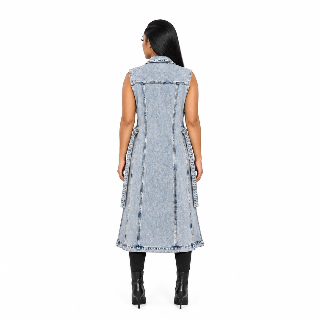 A woman viewed from the back wearing a sleeveless, light-wash denim midi dress with fringe trim and tie details at the sides, paired with black boots, against a plain white background.