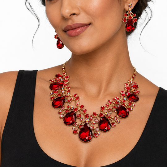 A woman wearing a red and gold statement necklace with matching drop earrings, styled with a black tank top against a plain white background.
