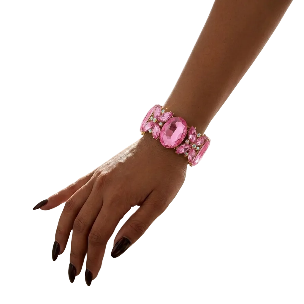 A close-up lifestyle shot of a woman's hand resting on a white marble vanity table, wearing a wide pink rhinestone bracelet.