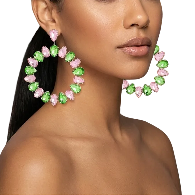 Woman wearing large hoop earrings with pink and green stones in a luxurious room.