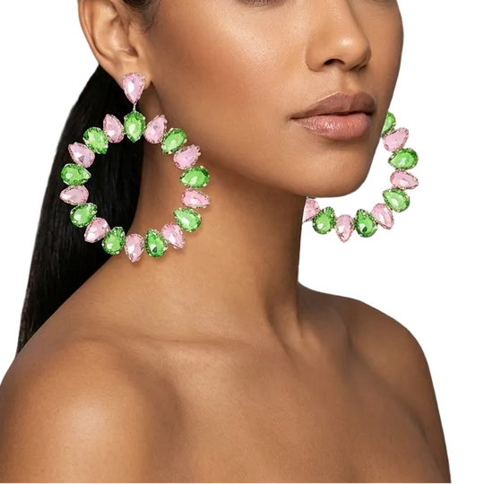 Woman wearing large hoop earrings with pink and green stones in a luxurious room.