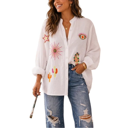 Woman wearing a white embroidered shirt and blue jeans in an art studio.