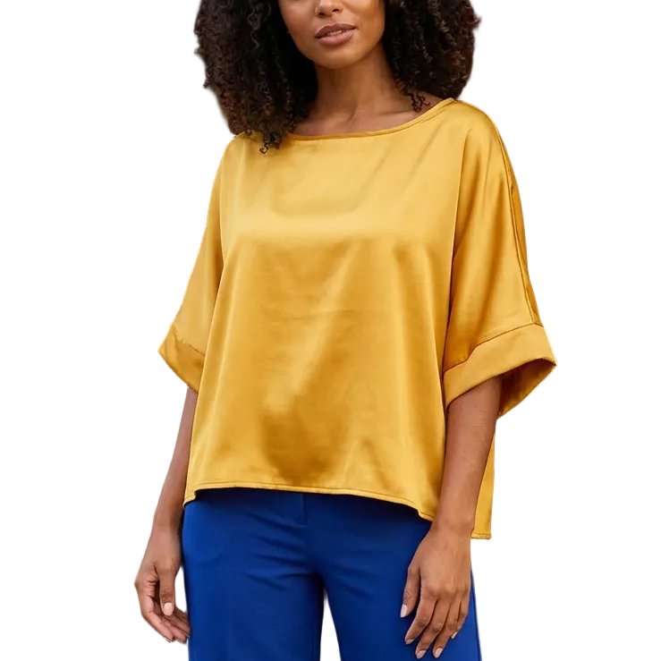 Woman wearing a yellow top and blue pants standing in front of a building entrance.