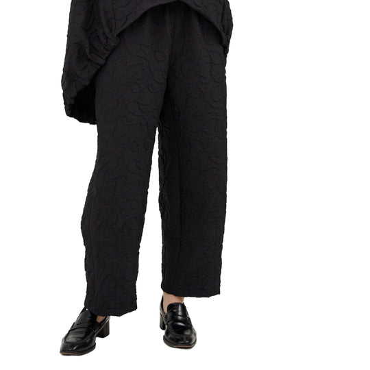 Person wearing black textured pants and shoes on a white background