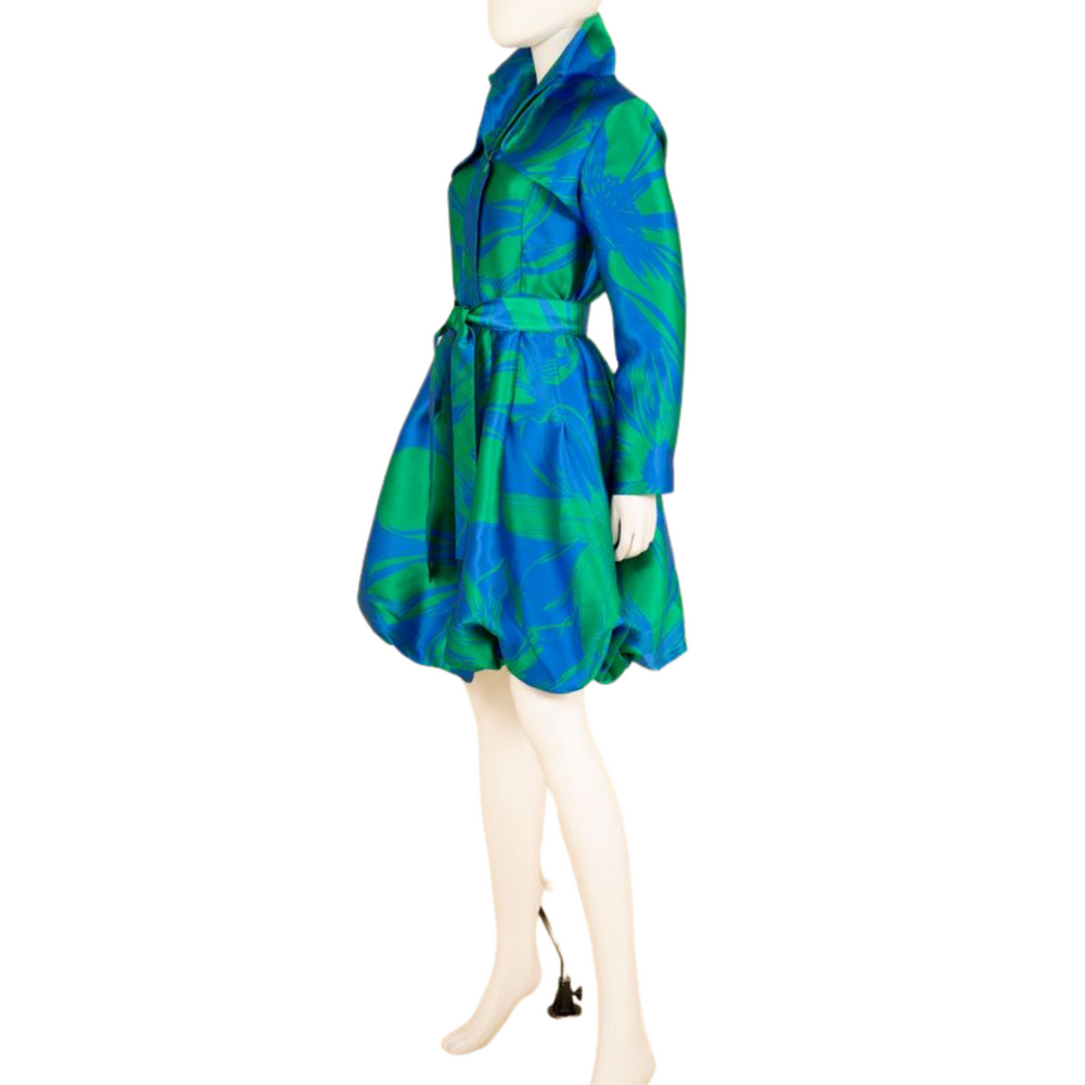 A mannequin displaying a blue and green jacquard dress coat with a wired collar, belt, and pockets.