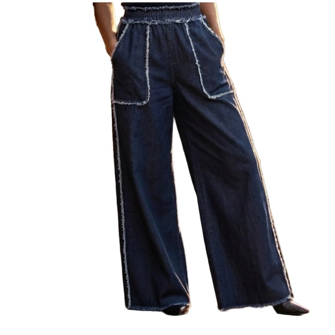 Person wearing blue wide-leg pants with white trim standing against a brick wall.