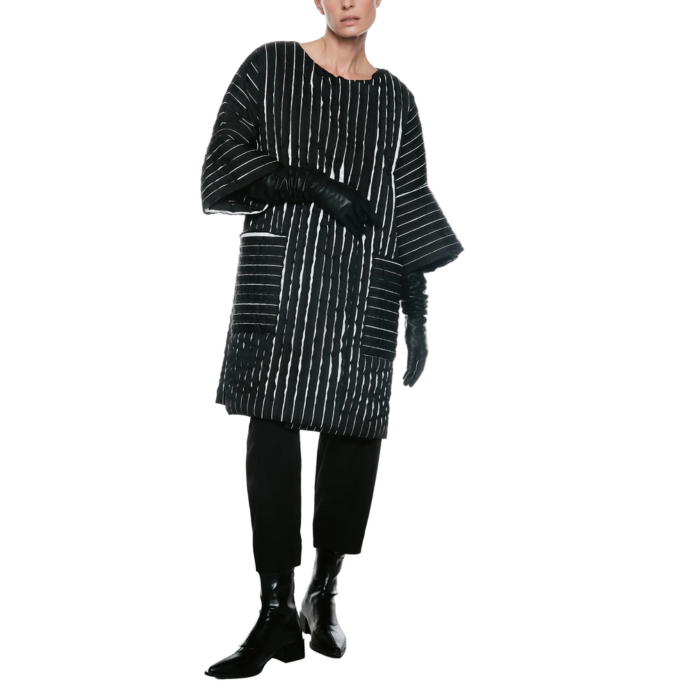 A model wearing a black and white vertically striped oversized tunic top with wide draped sleeves, paired with black pants and black leather ankle boots, against a plain white studio background.