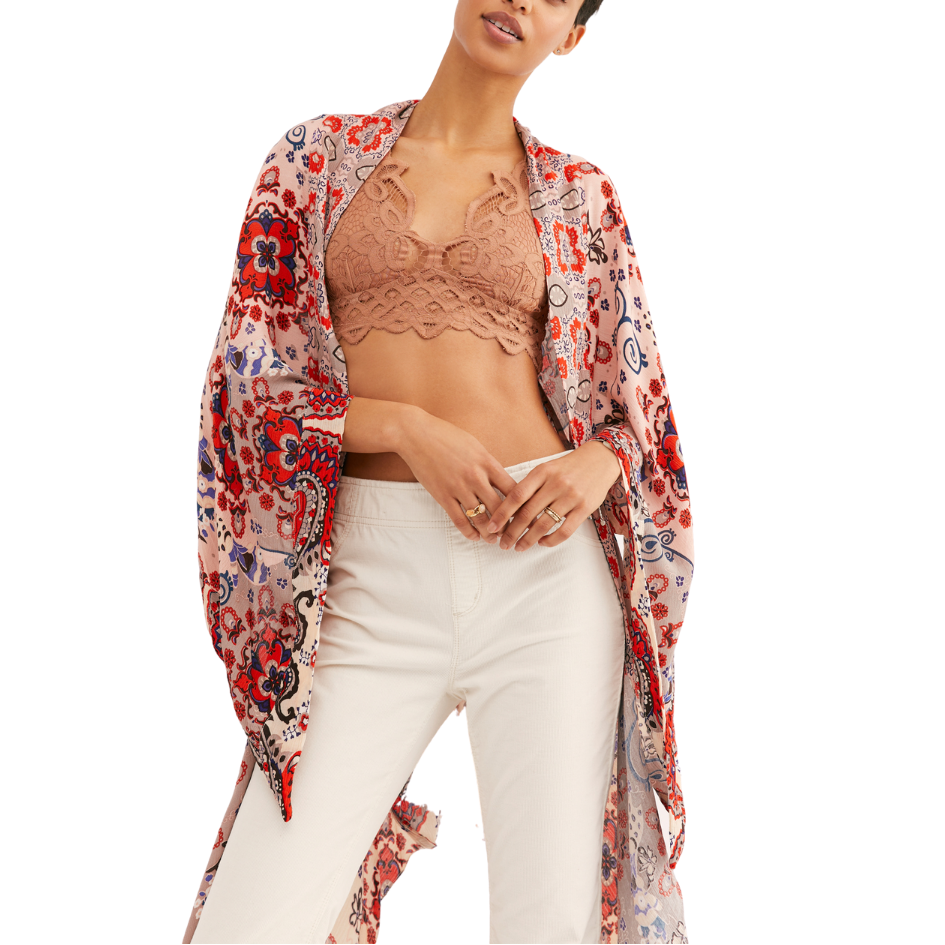 A woman wearing a red and multicolor floral kimono with an asymmetrical hem and back cutout details, paired with white pants.
