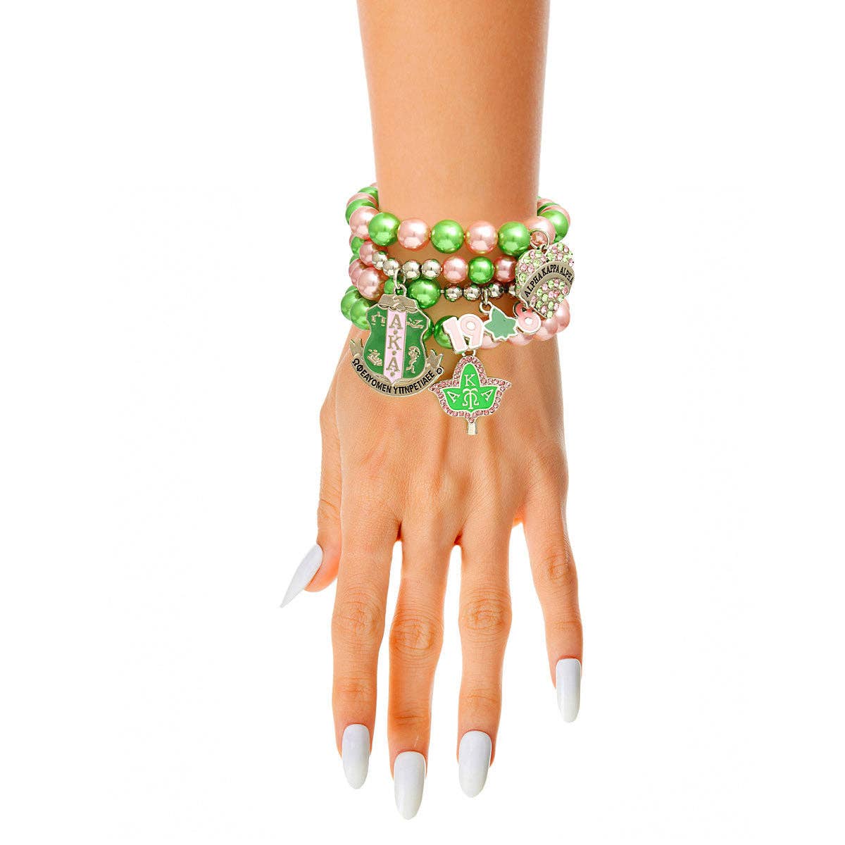 A person's hand wearing a stack of bracelets with pink and green pearls, silver metal accents, and rhinestone charms including a shield and a heart.
