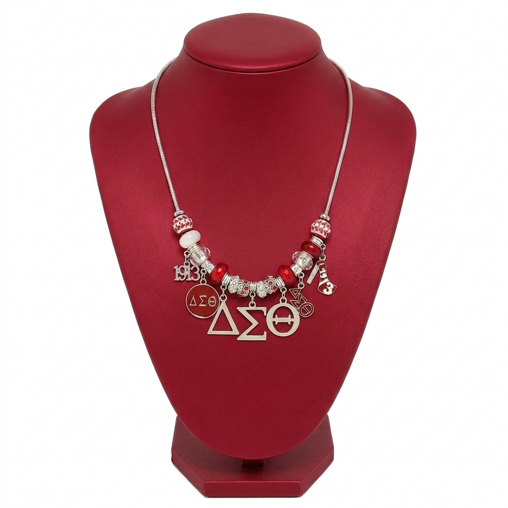A red and silver beaded charm necklace displayed on a red jewelry bust. The necklace features red and white beads, silver-toned metal, and Greek letter charms including Delta Sigma and Theta.