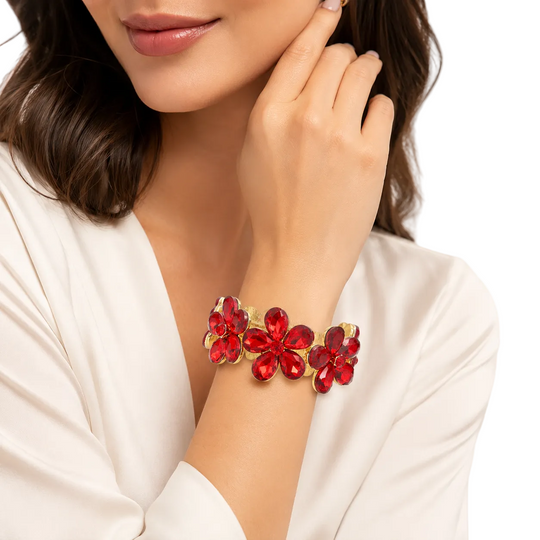 A close-up of a woman wearing a gold-tone cuff bracelet adorned with red flower-shaped crystals, set against a clean white background.