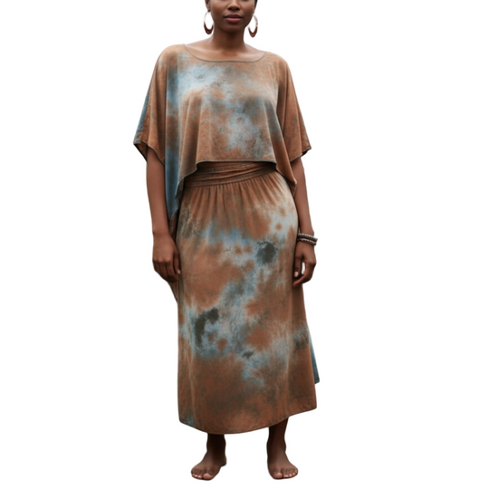 Woman in a tie-dye dress standing in a greenhouse filled with plants.