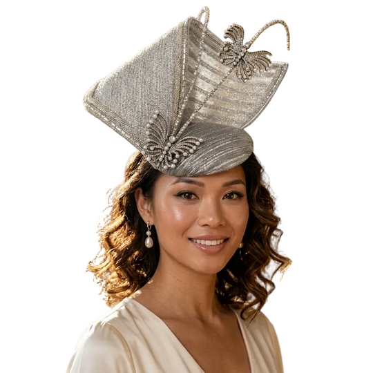 A woman wearing an ornate silver fascinator hat with butterfly embellishments, photographed in a softly blurred indoor event setting with warm lighting.