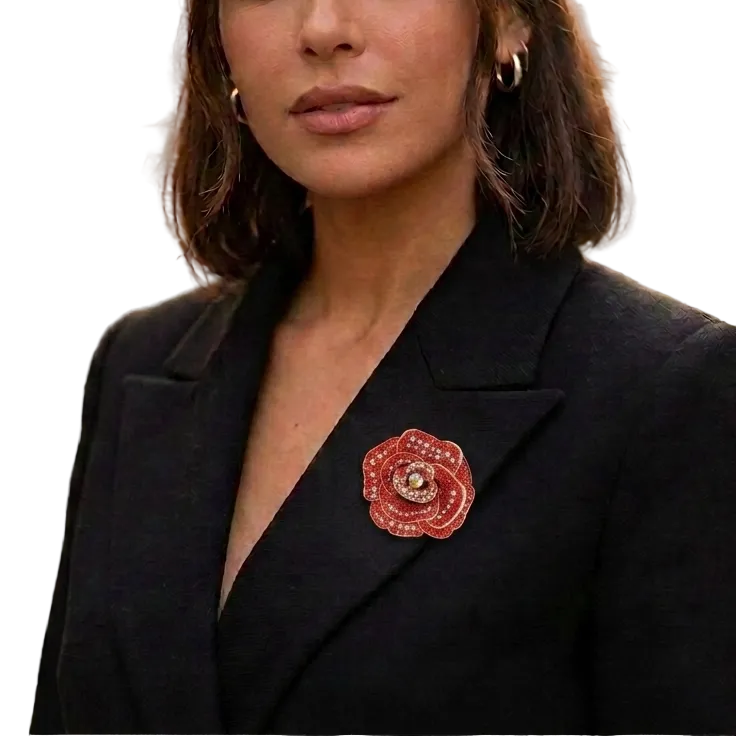 A woman wearing a black blazer and small hoop earrings, with a red rose-shaped brooch pinned to her blazer, photographed outdoors on a blurred city street.
