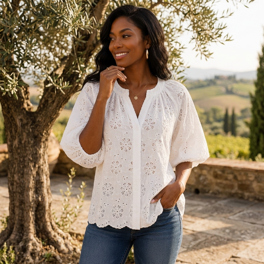 Woman wearing a white blouse with floral patterns in a scenic outdoor setting.