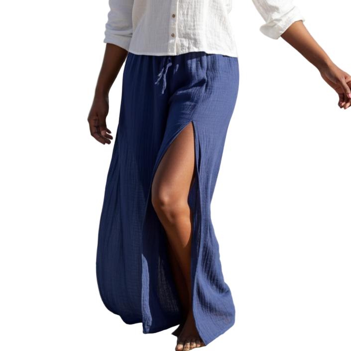 Woman walking on a beach wearing a white blouse and blue skirt.