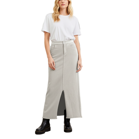 Woman wearing a white t-shirt and light gray skirt standing in a room with large windows.