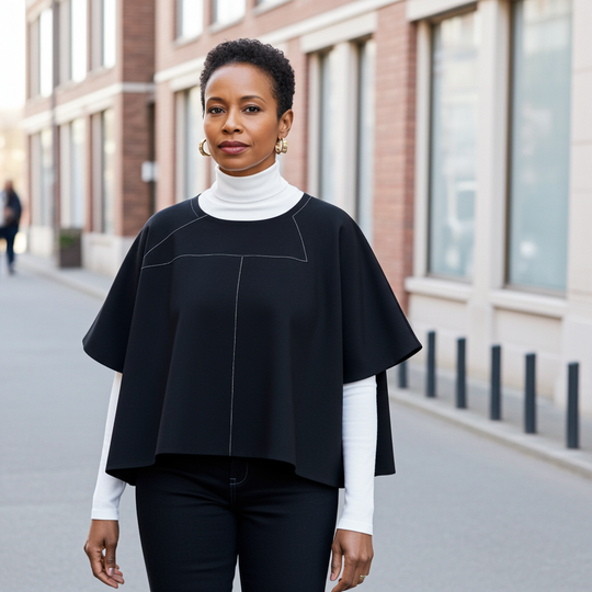 Woman wearing a black poncho over a white turtleneck in an urban setting
