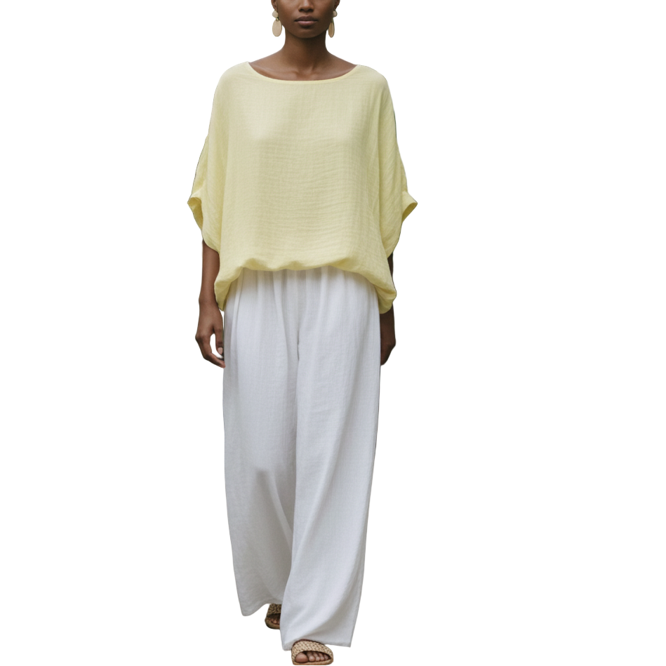 Woman in a yellow top and white pants standing among green plants