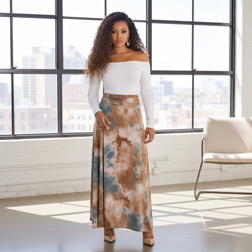 Woman wearing a white top and tie-dye skirt standing in a room with large windows.