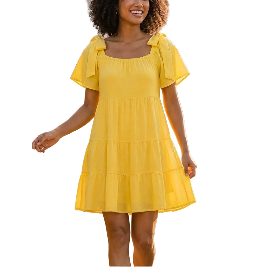 Woman in a yellow dress standing in a garden with flowers and a building in the background