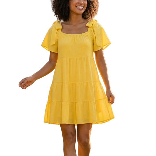 Woman in a yellow dress standing in a garden with flowers and a building in the background