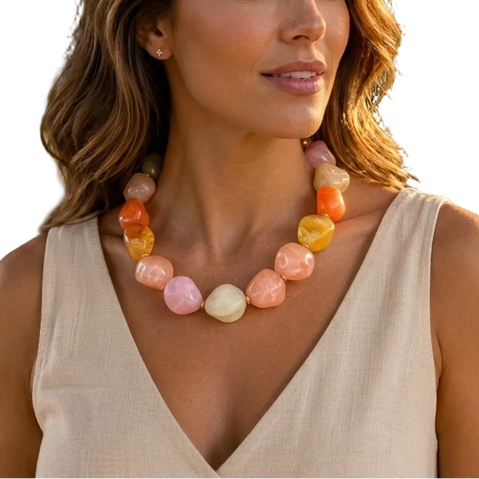 Woman wearing a colorful necklace outdoors with trees and flowers in the background