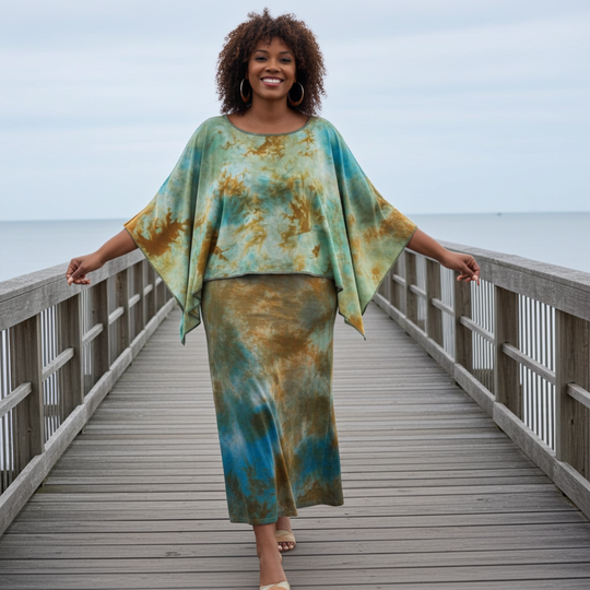 Woman in a tie-dye outfit standing on a wooden pier by the ocean.