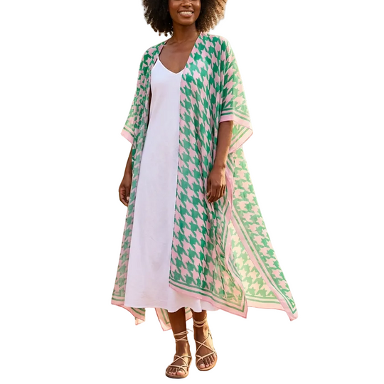 Woman in a white dress and green patterned cover-up standing on a wooden path in a garden.