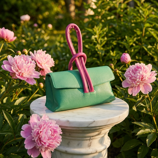 Green handbag with pink handle on a pedestal surrounded by pink flowers
