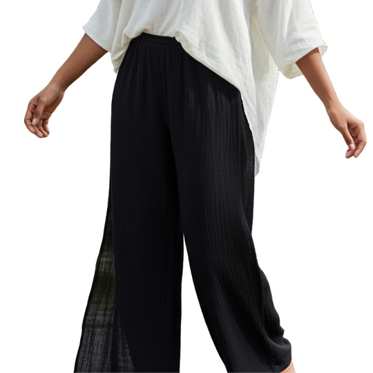 Woman in a white top and black pants standing in a garden with plants and water in the background