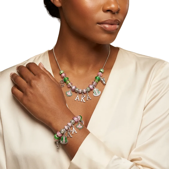 Woman wearing a necklace and bracelet with 'AKA' charms against a blurred natural background