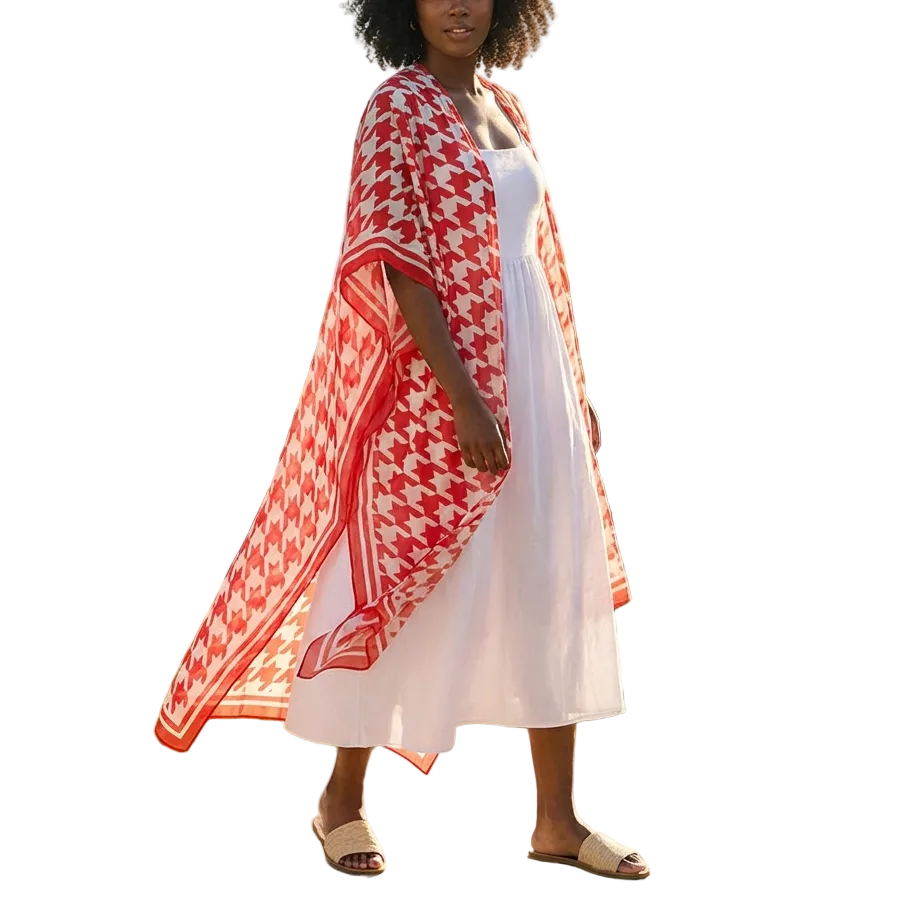 Woman in a white dress with a red patterned cover-up standing outdoors with a scenic background.