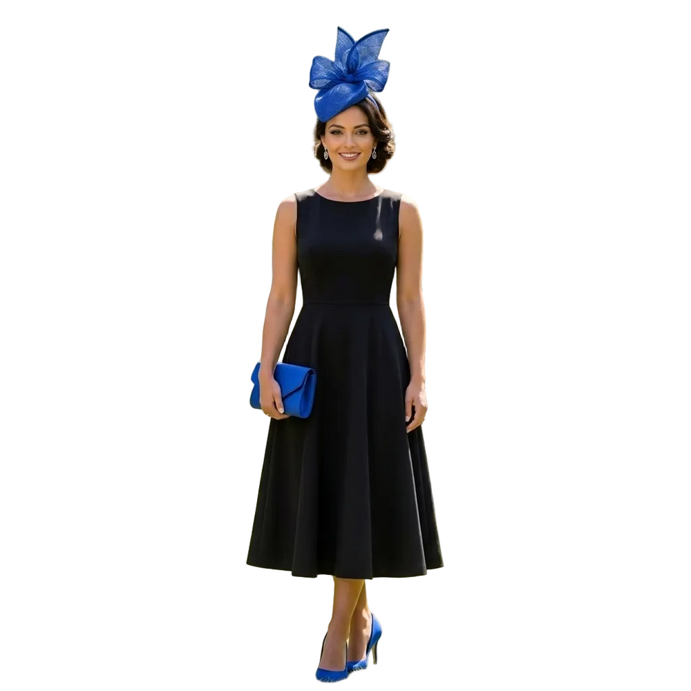 Woman in a black dress with a blue fascinator and clutch standing in a garden.