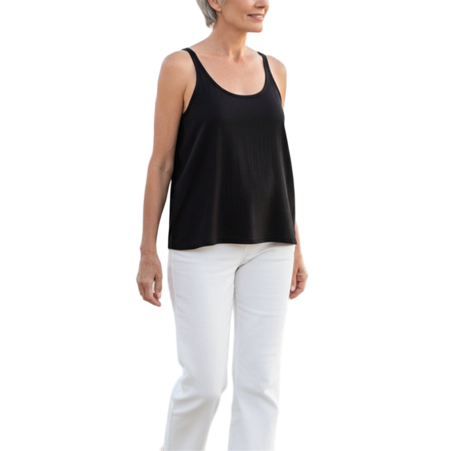 Woman standing on a beach wearing a black tank top and white pants.