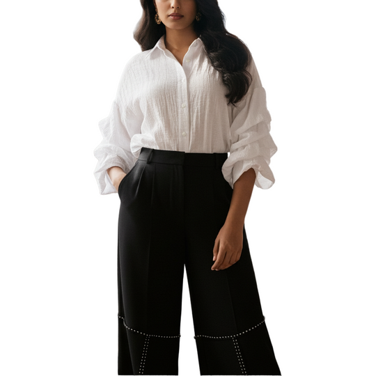 Woman wearing a white blouse and black pants standing in a room with large windows.