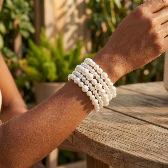Person wearing multiple pearl bracelets on a wooden surface with a blurred natural background