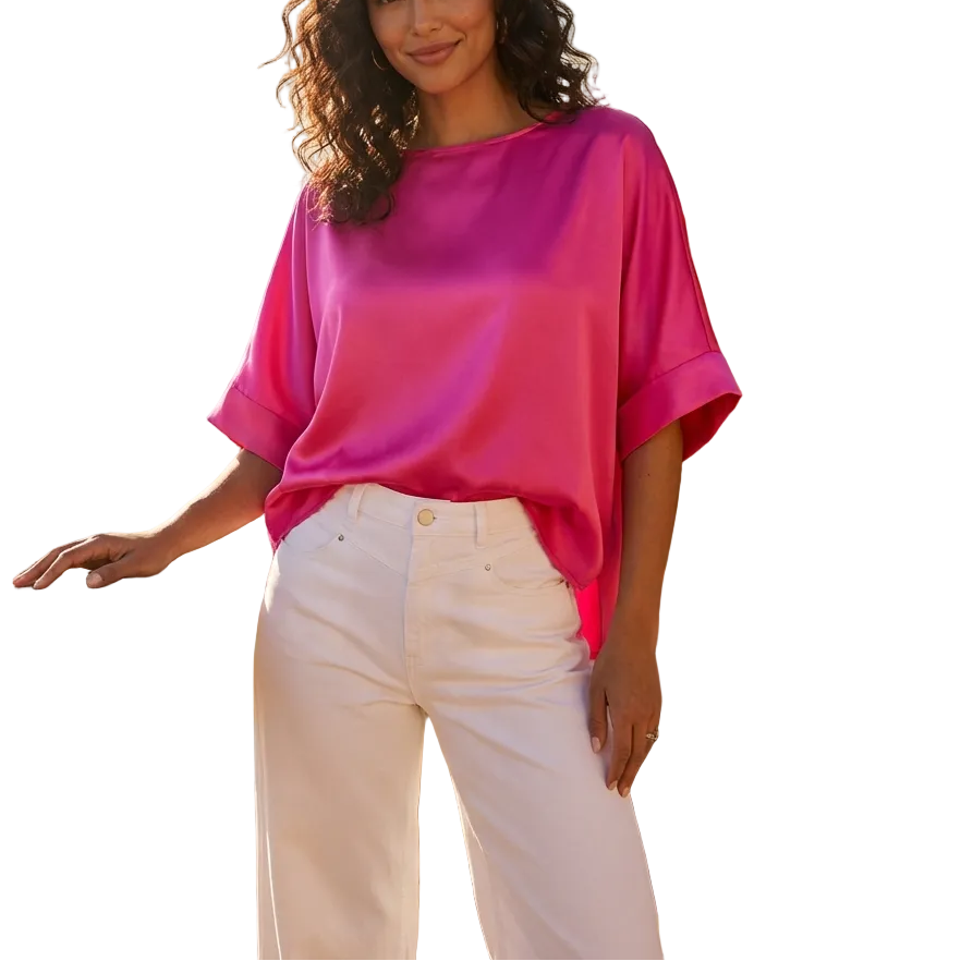 Woman wearing a bright pink top and white pants standing on a balcony with flowers and water in the background