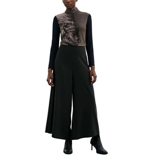 Woman in a long black dress with a patterned top on a rooftop with city skyline in the background