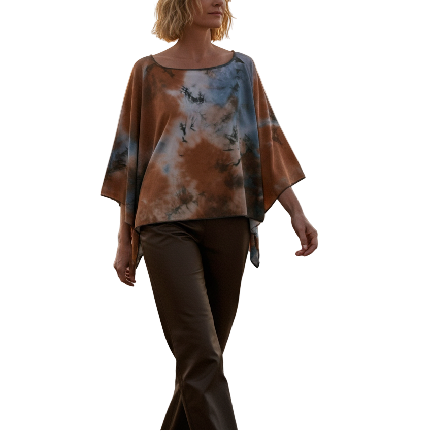 Woman walking on a beach at sunset wearing a tie-dye shirt and brown pants.