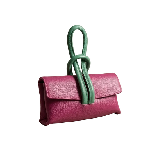 Pink handbag with a green handle on a beige surface