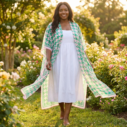 Woman walking outdoors in a garden wearing a green and pink and white patterned kimono-style garment.