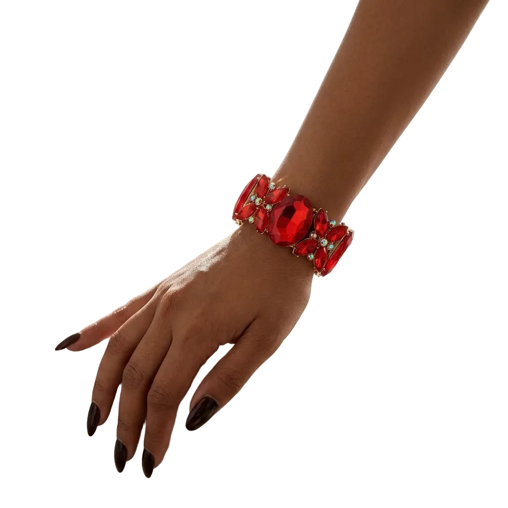 A close-up lifestyle shot of a woman's hand resting on a white marble vanity table, wearing a chunky red crystal bracelet with small clear rhinestone accents.