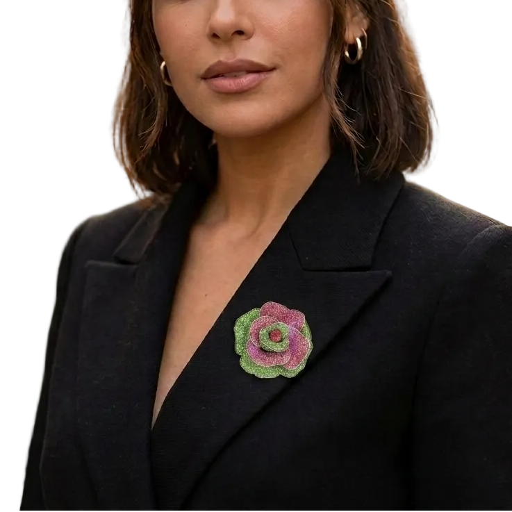 A close-up of a woman wearing a black blazer and gold hoop earrings, featuring a pink and green textured fabric rose brooch pinned to the left lapel.