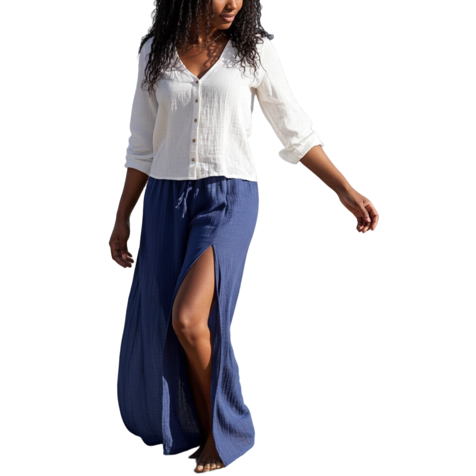 Woman walking on a beach wearing a white blouse and blue skirt.
