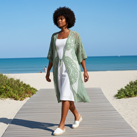 Woman walking on a wooden path by the beach wearing a green kimono and white dress.
