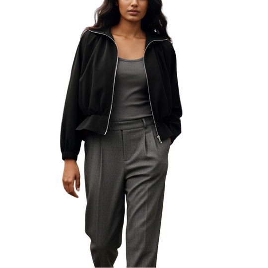 Woman in a black jacket and gray outfit walking through a greenhouse filled with plants.