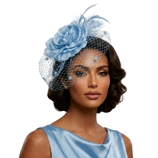 A woman wearing a light blue fascinator hat with a large fabric flower, feather, and net veil, paired with a matching light blue satin dress against a plain light background.