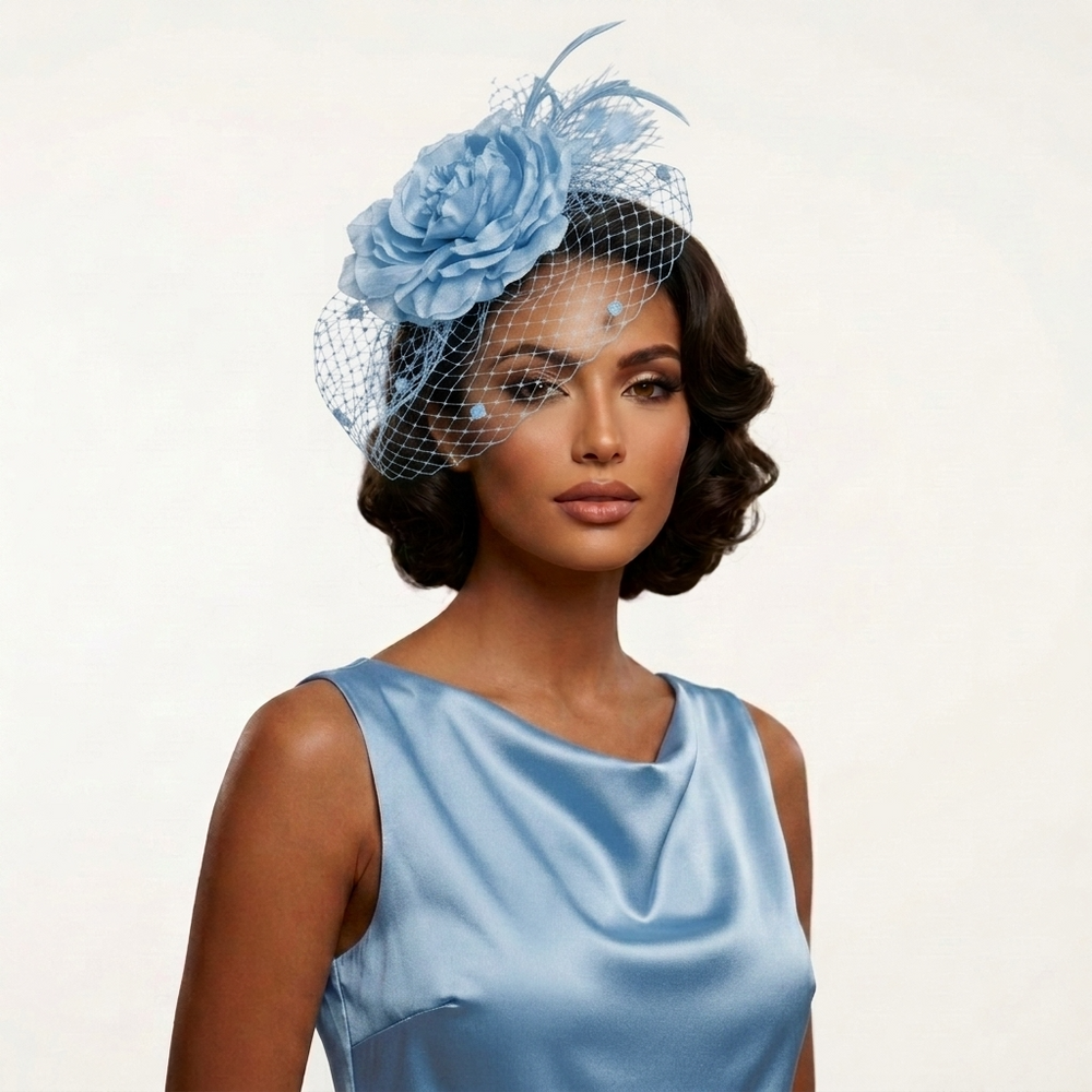 A woman wearing a light blue fascinator hat with a large fabric flower, feather, and net veil, paired with a matching light blue satin dress against a plain light background.