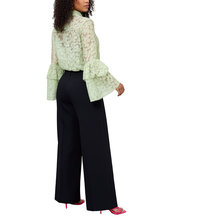 Woman in a light green blouse and black pants standing in front of an abstract painting.